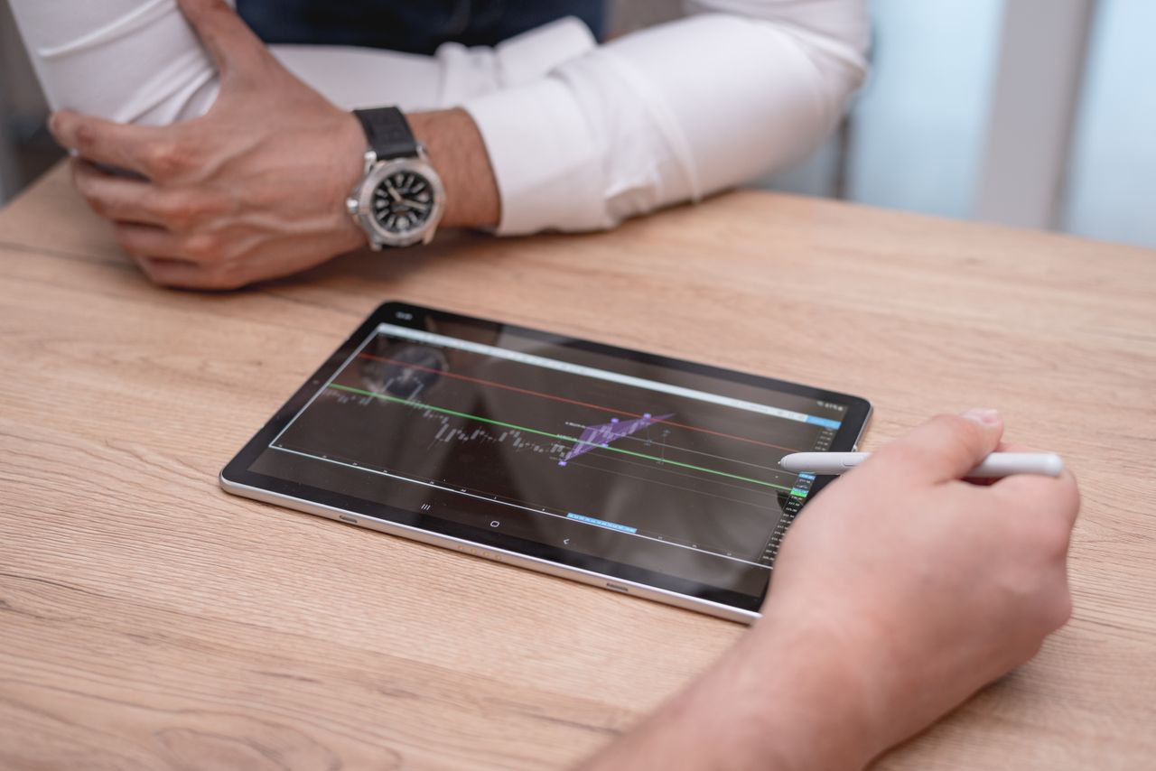 Close-up of hands using a digital tablet with trading charts on a wooden desk.