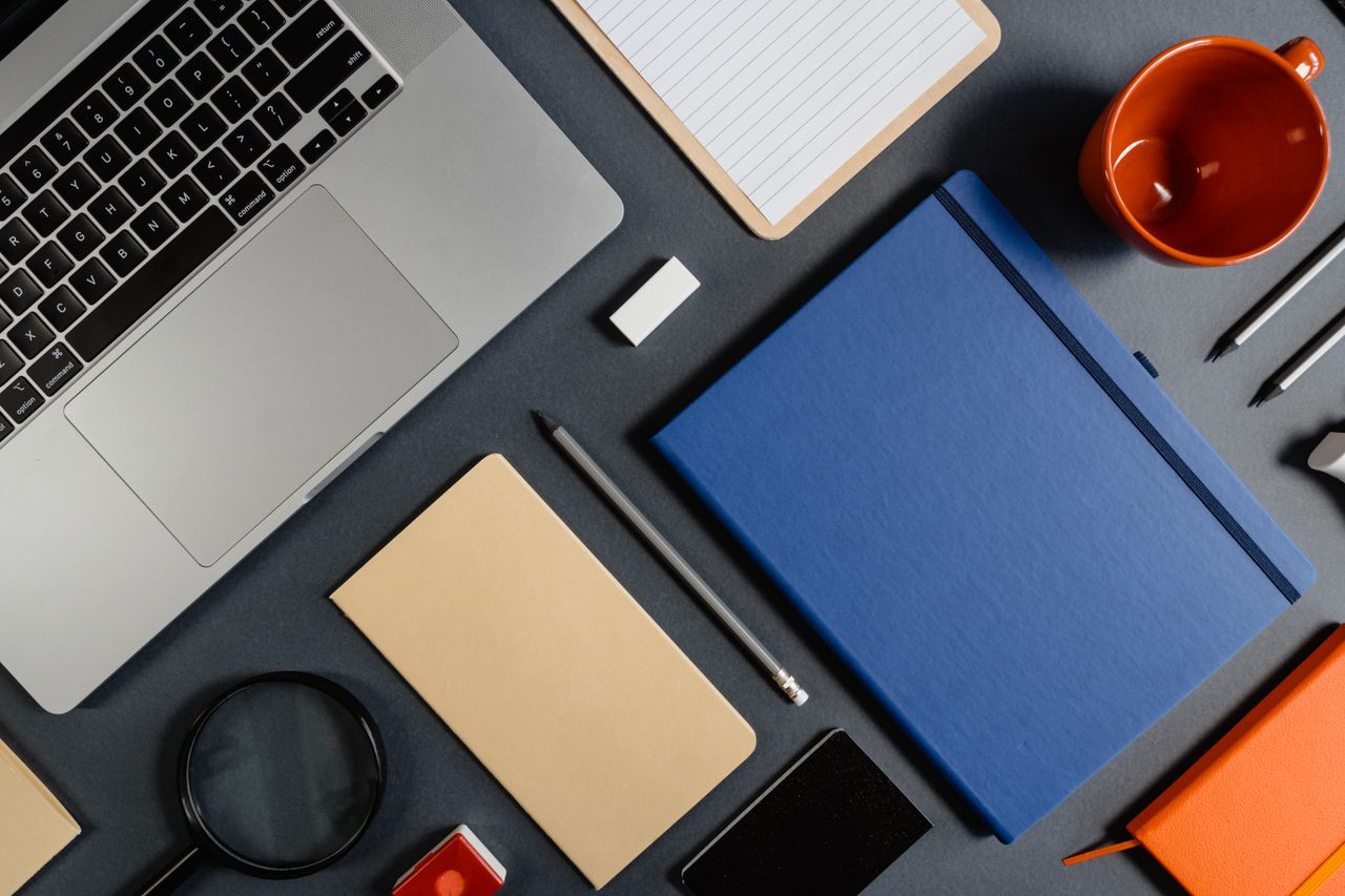 Top view of a tidy workspace with a laptop, notebooks, and office supplies arranged neatly.